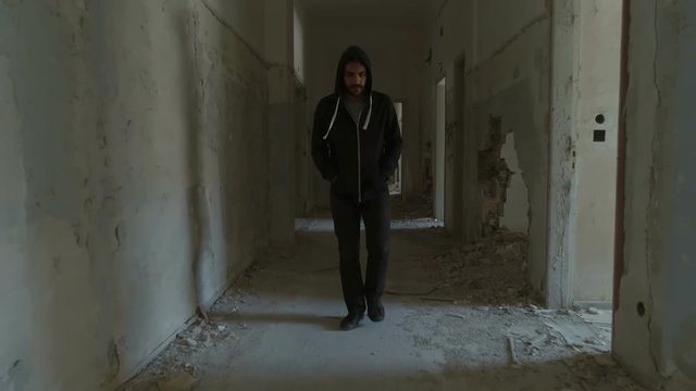 Hooded young man inside destroyed abandoned building,slow motion,dramatic.A sad young man facing social issues, walking inside a big wrecked empty building in slow motion.Drone/dolly motion.