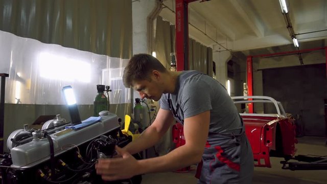 Mechanic working on classic car engine in restoration workshop