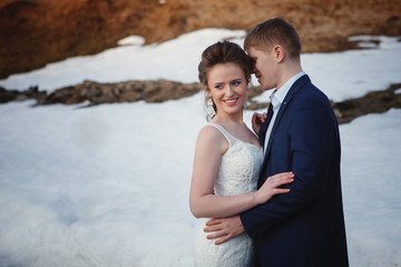 Winter wedding outdoors on snow background. Bride and groom are standing and hugging.