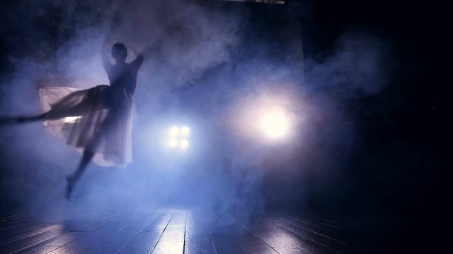 A female dancer rushes through a dark stage. 