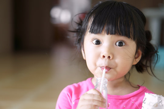 Asian Children Cute Or Kid Girl Drinking Water Or Soy Milk Beverage In Bottle By Tube And Eating Snack Or Dessert With Make Funny Or Joke Face And Big Eye For Enjoy And Wearing Pink Shirt With Space