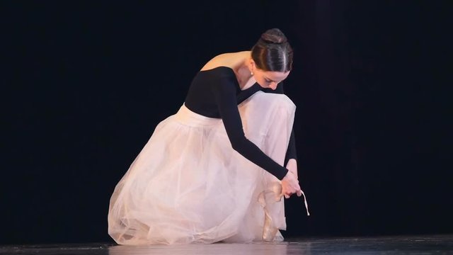 A ballerina ties up her white shoe.  