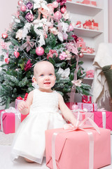 Christmas evening. Little girl sitting and unwraps gifts. white dress Princess