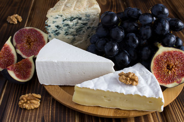 Cheeses, black grapes and figs on the wooden round cutting board