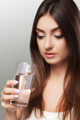 Young girl drinks water. Healthy look of the face. Portrait of a girl. The concept of beauty and health. On a gray background.