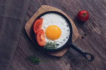 Scrambled eggs in a cast-iron frying pan with tomatoes on a wooden dark table.