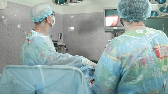 Surgeons follow the laparoscopic surgery, looking at screen