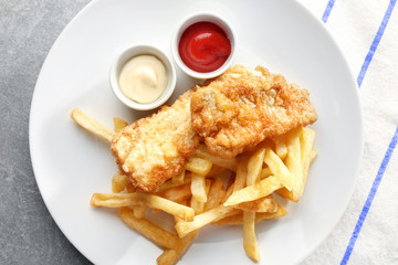 Plate with tasty fried fish, chips and sauces on table
