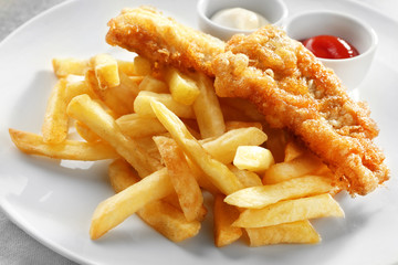 Tasty fried fish, chips and sauces on plate, closeup