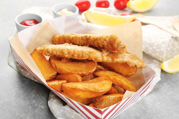Paper box with tasty fried fish and chips on table