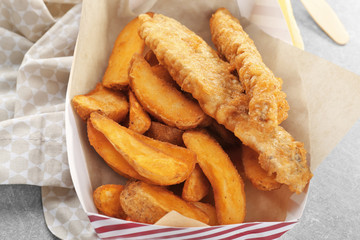 Paper box with tasty fried fish and chips on table, closeup