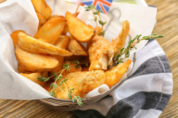 Basket with tasty fried fish and potatoes on wooden table