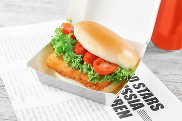 Sandwich with tasty fried fish in paper box on table