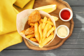 Tasty fried fish and chips rolled in paper on wooden table
