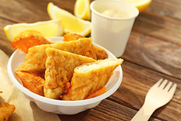 Plastic plate with tasty fried fish and potatoes on table