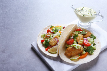Marble board with tasty fish tacos and sauce on table