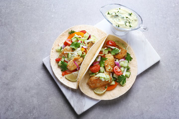 Marble board with tasty fish tacos and sauce on table