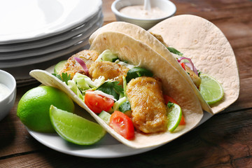Plate with tasty fish tacos on wooden table