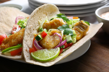 Plate with tasty fish tacos on wooden table