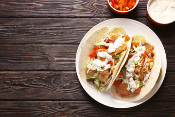 Plate with tasty fish tacos and sauce on wooden table