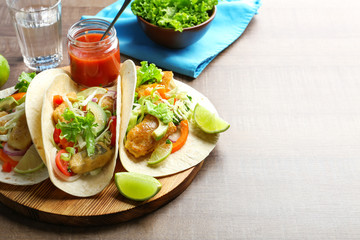 Wooden board with tasty fish tacos on table