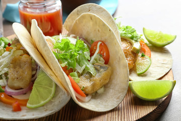 Wooden board with tasty fish tacos on table