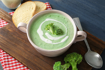 Plate with delicious broccoli cheese soup and slices of bread on wooden board