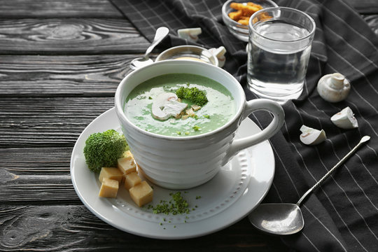 Cup with delicious broccoli cheese soup and croutons on wooden table