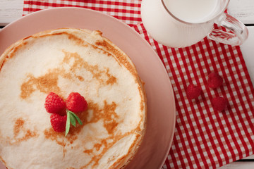 Stack of thin pancakes served with raspberry on pink plate