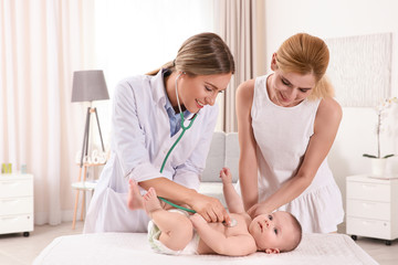 Doctor examining baby with stethoscope at home