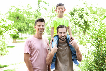 Male gay couple with foster son having fun in park. Adoption concept