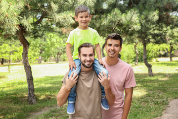 Fototapeta premium Male gay couple with foster son having fun in park. Adoption concept