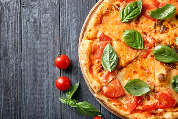 Delicious pizza with cherry tomatoes and fresh basil on kitchen table