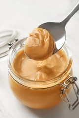 Spoon and glass jar with creamy peanut butter on light background