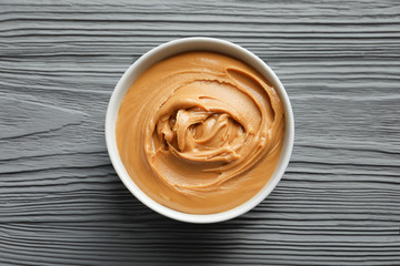 Ceramic bowl with creamy peanut butter on wooden background