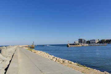 Fototapeta premium Bay view of the port town of Tomis, Constanta. Small Constanta harbour gateway view. Sea wall for protect the beach. Breakwaters concrete tetra-pods. 