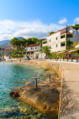 Naklejka premium Chairs with tables of coastal bar on rocks and view of shore in Bol town, Brac island, Croatia.