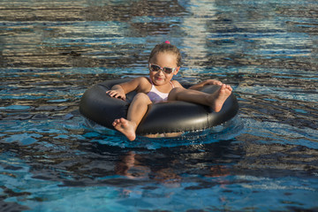 Happy little girl playing with inflatable ring in outdoor swimming pool on hot summer day. Kids learn to swim. Child water toys. Children play in tropical resort. Family beach vacation.
