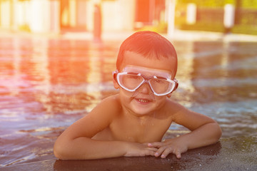 A happy young boy relaxing on the side of a swimming pool wearing goggles. Toned