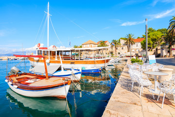Fototapeta na wymiar Fishing boats and chairs of local cafe bar in Sutivan port, Brac island, Croatia