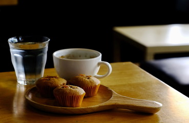 Snacks during breaks,There is a small cupcake in wooden tray and black coffee in white glass as cool drinking water on the table in the corner of the room.