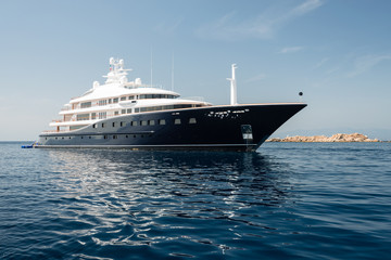 Large luxury motor yacht anchored near rocky island