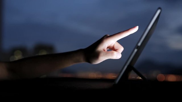 Woman finger touching tablet touchscreen at night time.
