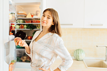 Cute female in pajamas taking peach from the fridge, attractive housewife take care about health, fresh tasty organic food, healthy eating concept.