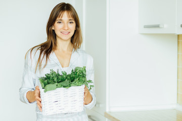 Healthy eating, cooking, vegetarian food, dieting and people concept - close up of young woman with green vegetables in white backet in kitchen interior.