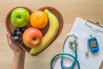 Cholesterol diet and healthy food nutritional concept with clean fruits in heart dish with nutritionist monitoring, blood sugar control record with measuring tool kit