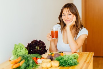 Obraz na płótnie Canvas Healthy brunette woman drinking fresh detox Jjuice, Smoothie for breakfast. Closeup of beautiful smiling girl with vegetables at kitchen table. Nutrition concept.