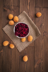 Delicious ripe apricots and raspberries on a wooden background, burlap cloth. Horizontal top view