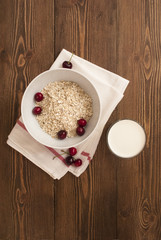 Bowl, bran, milk and fresh cherries, on wooden background, top view