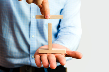 Man holds in his hands wooden blocks. Businessman builds figures using wooden blocks like structure based on pillars, metaphor for stability, reinforcement, concept.